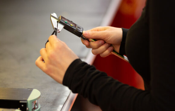Worker measuring machine part using digital calipers as part of the reverse engineering process