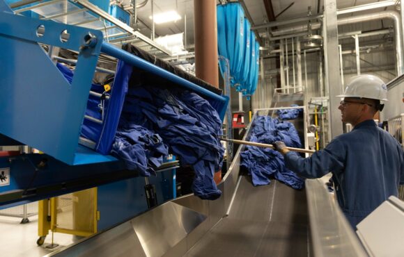 Worker unloading garments from hopper onto conveyor belt