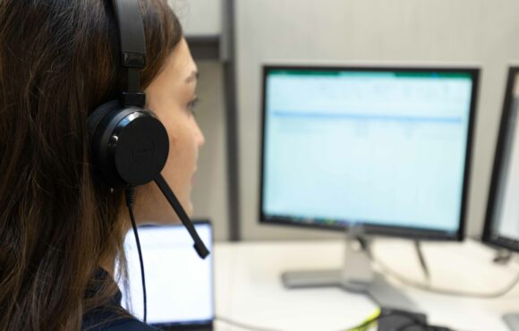 A worker wearing headphones and a mic looking at a computer screen