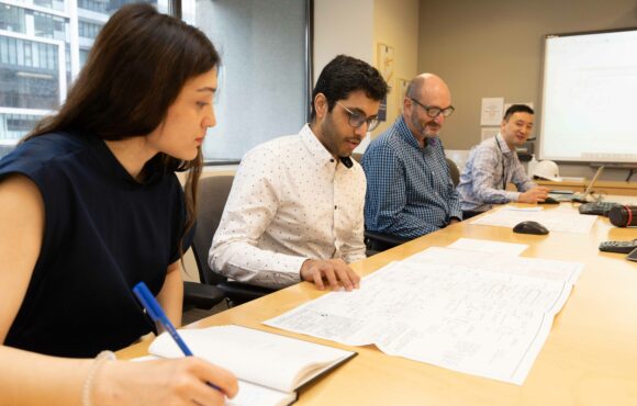 Four workers sitting in a line along a table, working on documents
