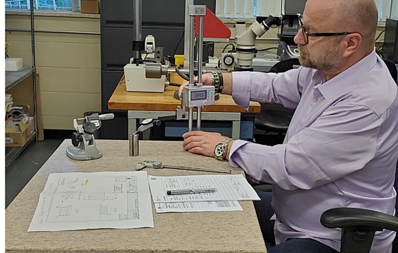 Worker measuring a component and noting the results on paper